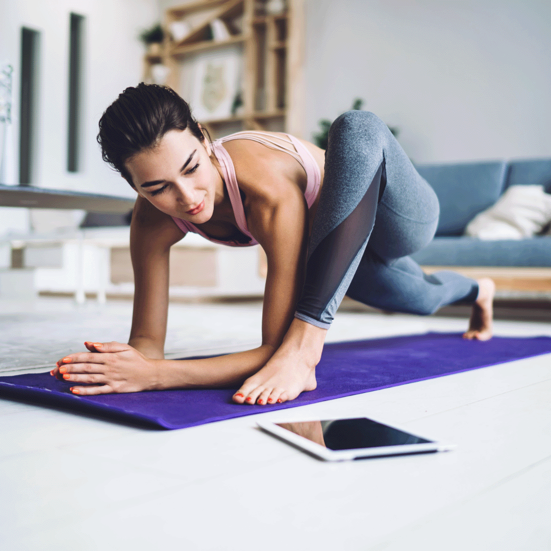 A woman practicing yoga at home, watching the instructor on an iPad