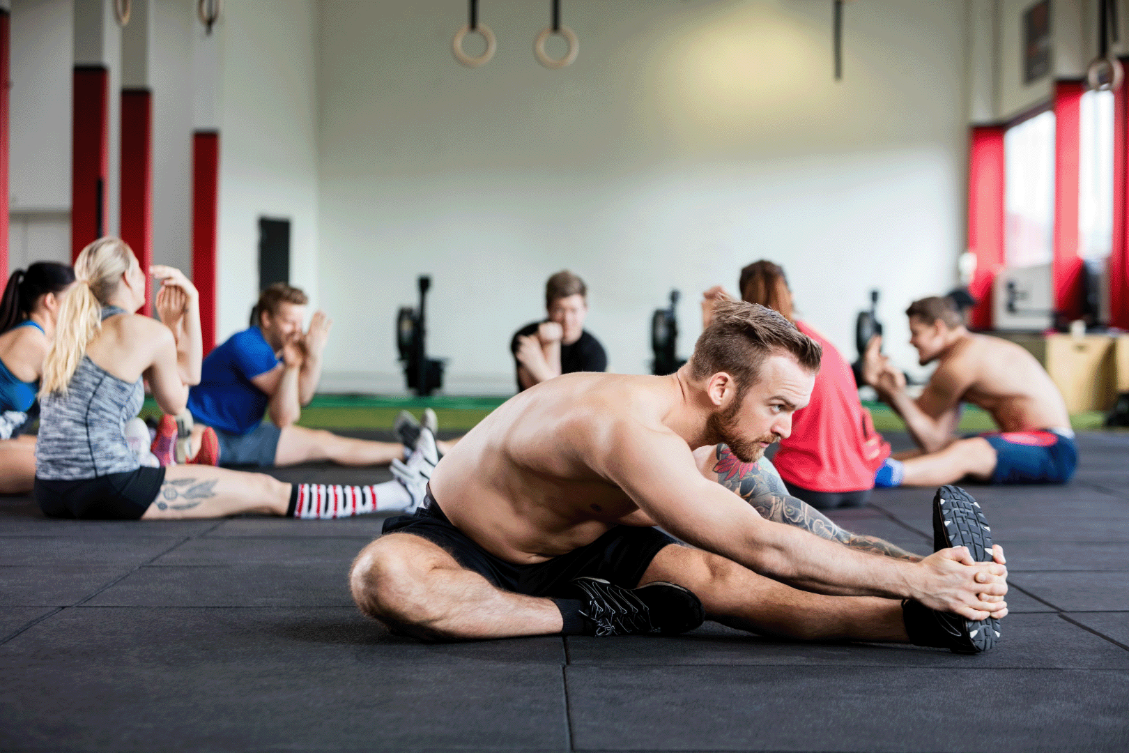 seven people, men and women, in a group stretching session in a gym, stretching their hamstrings