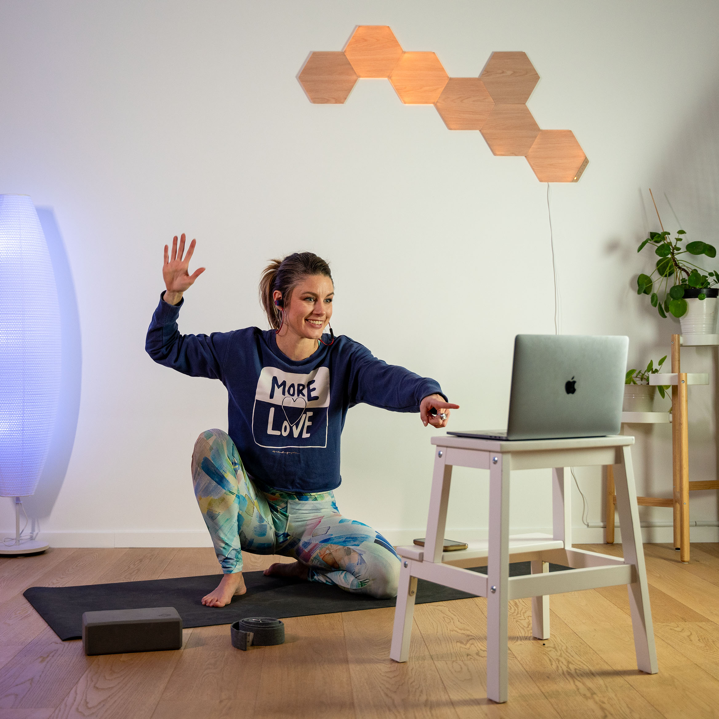  Klara Bright kneeling on her mat and pointing a finger to the screen of her laptop to congratulate her students during their online group yoga session